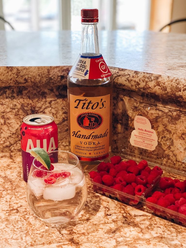 raspberry summer spritzer | Raspberry Spritzer by popular Pittsburg lifestyle blog, Fashionably Late: image of Titos handmade vodka, raspberries, AHA seltzer water and a raspberry spritzer in stemless glass with a lime wedge garnish. 