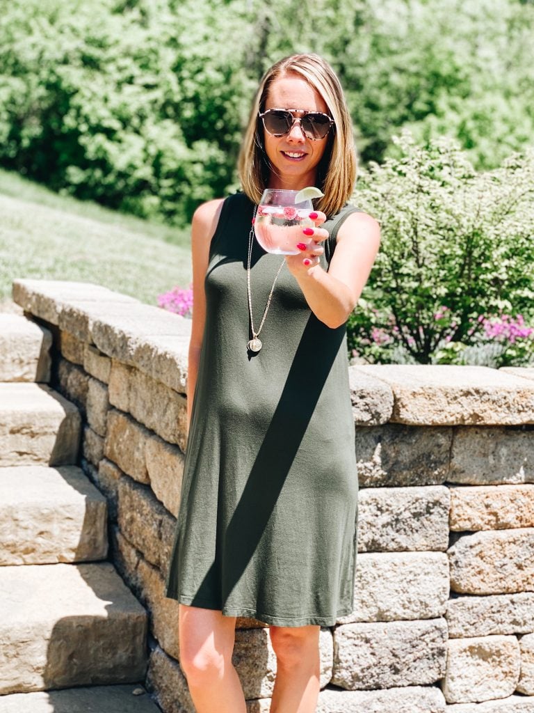 raspberry summer spritzer | Raspberry Spritzer by popular Pittsburg lifestyle blog, Fashionably Late: image of a woman standing outside and wearing a sleeveless green dress and holding a raspberry spritzer in stemless glass with a lime wedge garnish. 