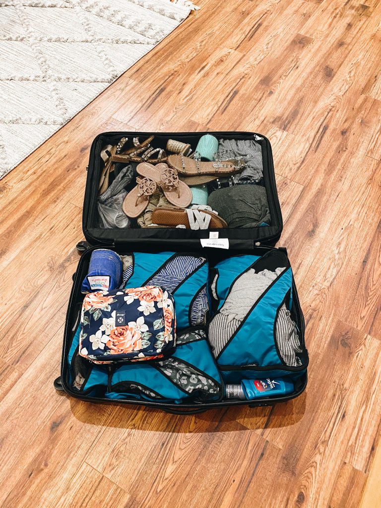 5 Top Packing Tips for your Family Vacation, featured by top Pittsburgh lifestyle blogger, Fashionably Late Mom. | Packing Tips by popular Pittsburgh travel blog, Fashionably Late Mom: image of a packed suitcase laying open on a wooden floor. 