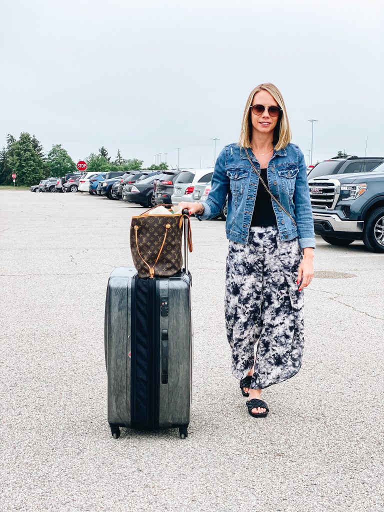 5 Top Packing Tips for your Family Vacation, featured by top Pittsburgh lifestyle blogger, Fashionably Late Mom. Packing can sometimes be stressful, but I've mastered it so it's not so bad. family vacation, luggage, how to pack, suitcase, samsonite | Packing Tips by popular Pittsburgh travel blog, Fashionably Late Mom: image of a woman wearing a denim jacket, black top, and black and white tie dye wide leg pants while pulling some rolling hard shell rolling luggage in a parking lot. 