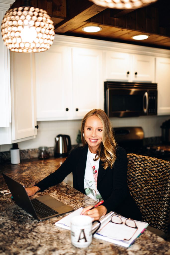 How to Style a Blazer by popular Pittsburgh fashion blog, Fashionably Late Mom: image of a woman wearing a floral graphic print t-shirt and black blazer while sitting at her kitchen counter next to her open laptop.