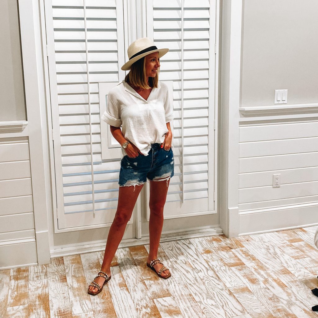 white linen top, distressed shorts, studded sandals, vacation outfits, 30A packing list, what to wear on vacation | 30A Packing List by popular Pittsburgh life and style blog, Fashionably Late Mom: image of a woman wearing a white linen top, distressed shorts, straw fedora hat, and brown studded strap sandals. 