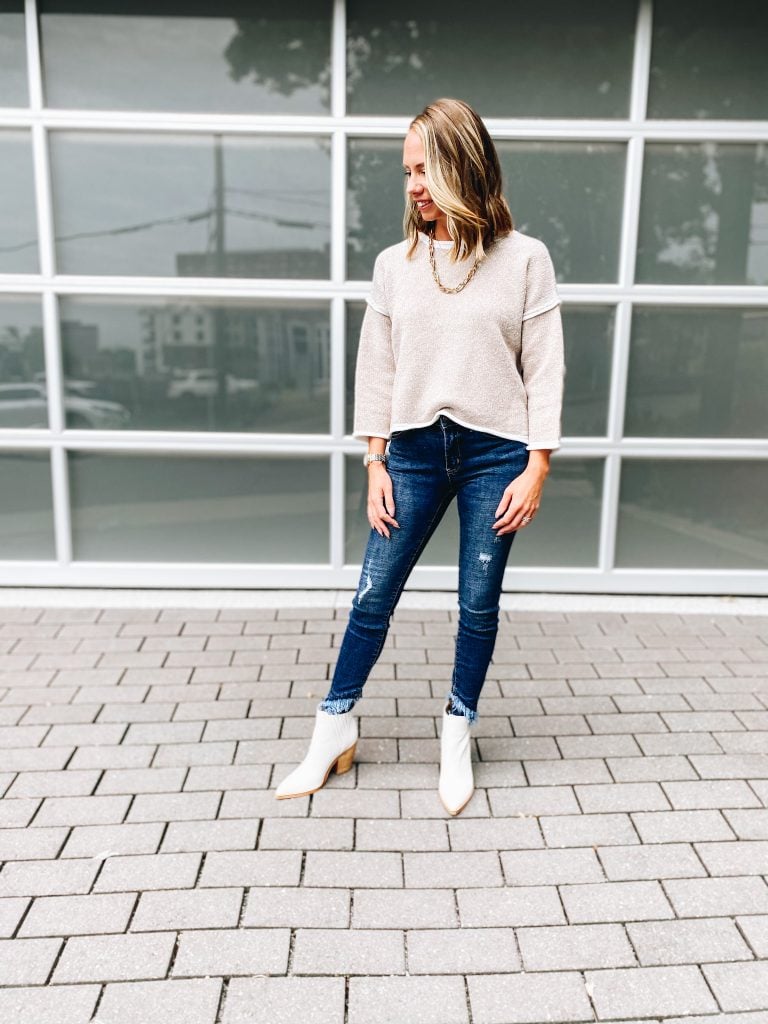 Pink Lily by popular Pittsburgh fashion blog, Fashionably Late Mom: image of a woman wearing a Pink Lilly  cream sweater, gold chain necklace, distressed jeans, and white ankle boots. 